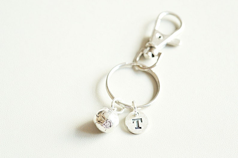May include: Silver keychain with a soccer ball charm and a letter 'T' charm.