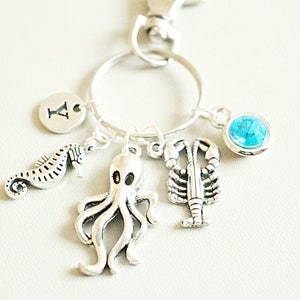 Könnte beinhalten: Silberner Schlüsselanhänger mit einem blauen Edelstein, einem Hummer, einem Oktopus, einem Seepferdchen und einem Anhänger mit dem Buchstaben A.