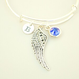 Puede incluir: Un brazalete de plata con un dije de cristal azul, un dije de ala de plata y un dije de plata con la letra "B" grabada.