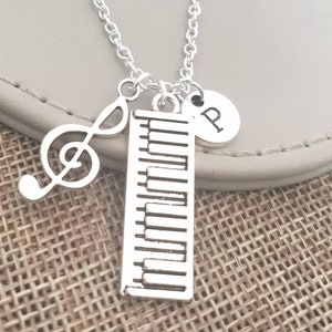 May include: Silver necklace with a piano keyboard charm, a treble clef charm, and a charm with the letter "P".
