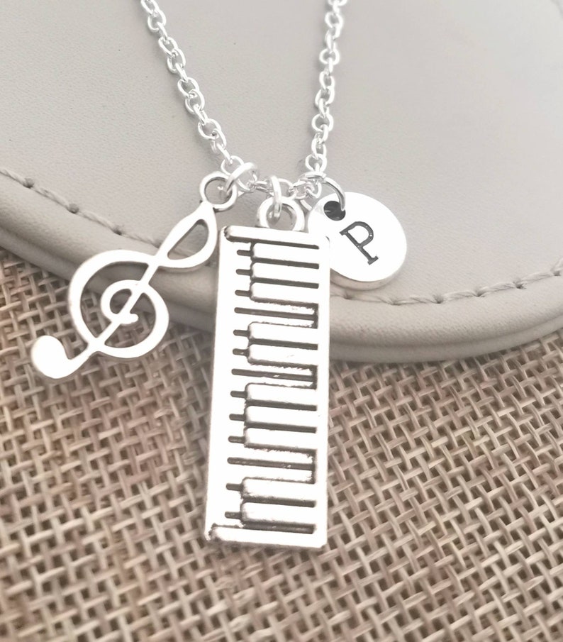 May include: Silver necklace with a piano keyboard charm, a treble clef charm, and a charm with the letter "P".