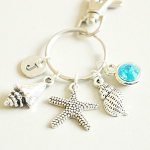 May include: Silver keyring with a blue crystal charm, two seashell charms, a starfish charm, and a letter "J" charm.