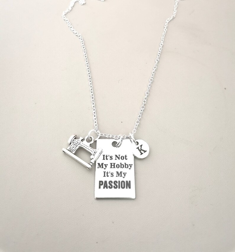 May include: Silver necklace with a sewing machine charm and a rectangular tag that reads "It's Not My Hobby It's My Passion". The necklace also has a charm with the letter "K" on it.
