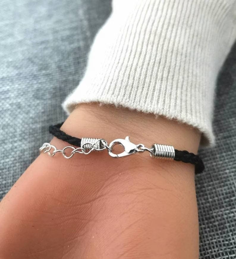 May include: A black braided bracelet with a silver clasp and a silver chain detail.
