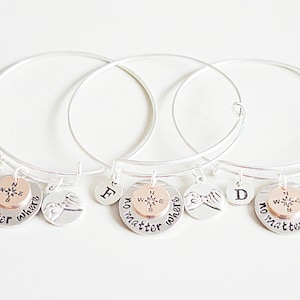 Puede incluir: Tres pulseras de plata con dijes. Cada dije tiene una brújula, una huella de mano y las letras B, F y D. Los dijes también tienen el texto "no matter where".