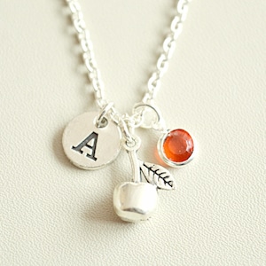 Puede incluir: Collar de plata con un dije de cereza, una pequeña piedra roja y un dije redondo con la letra A.