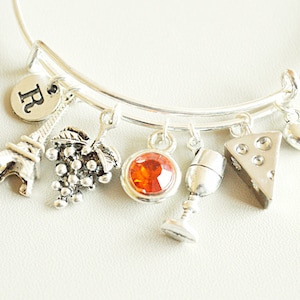 Peut inclure: Bracelet en argent avec des breloques, dont la tour Eiffel, des raisins, un verre à vin, un morceau de fromage, un cœur et un breloque avec la lettre "R".