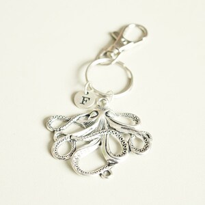 May include: Silver octopus keychain with a silver letter 'F' charm attached. The keychain has a silver lobster clasp.