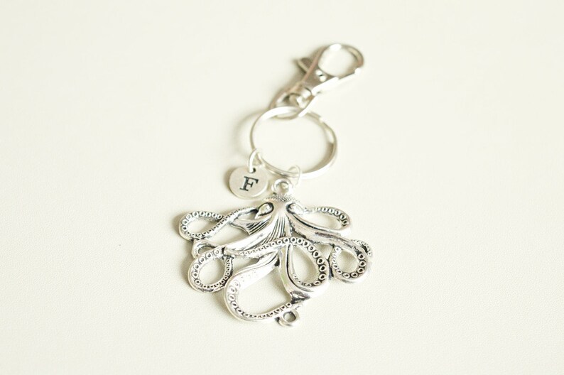May include: Silver octopus keychain with a silver letter 'F' charm attached. The keychain has a silver lobster clasp.