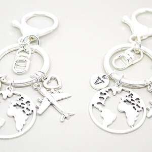 May include: Two silver keychains with a globe, airplane, heart, and letter charms. The letters on the charms are "I" and "A".