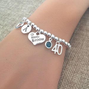 May include: Silver charm bracelet with a heart charm that says "Happy Birthday", a letter "A" charm, a blue gemstone charm, and a number "40" charm.