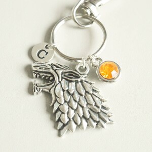 May include: Silver keychain featuring a wolf head charm with a textured design, a small letter "C" charm, and an orange crystal charm.