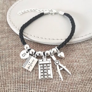 May include: Black braided bracelet with silver charms including a calculator, compass, heart, and a charm with the letter 'S' and the equation '4+2=22'.