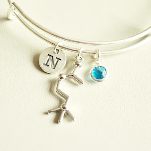 Puede incluir: Un brazalete de plata con un dije de plata que dice "N", un dije de plata que parece una estructura química y un dije de piedra preciosa azul claro.