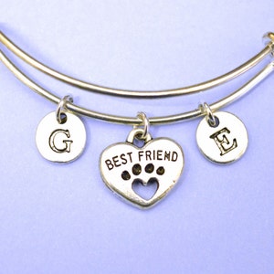 May include: Silver charm bracelet with a heart charm that says "Best Friend" with paw prints and a cut-out heart. The bracelet also has two charms with the letters "G" and "E" on them.