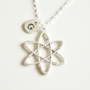 May include: Silver necklace with an atom charm and a small disc charm with the letter G.