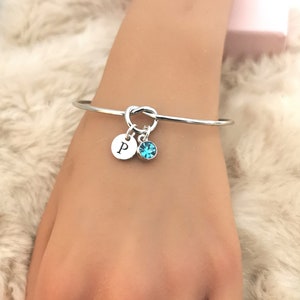 May include: Silver knot bangle bracelet with a charm featuring the letter "P" and a turquoise blue crystal.