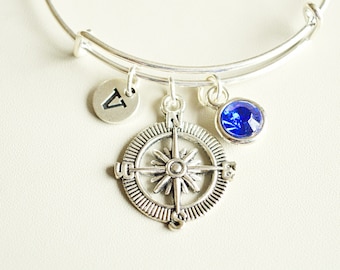 Puede incluir: Un brazalete de plata con un dije de brújula, un dije de cristal azul y un dije con la letra "V".