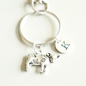 May include: Silver cow charm keychain with a silver initial charm with the letter K.