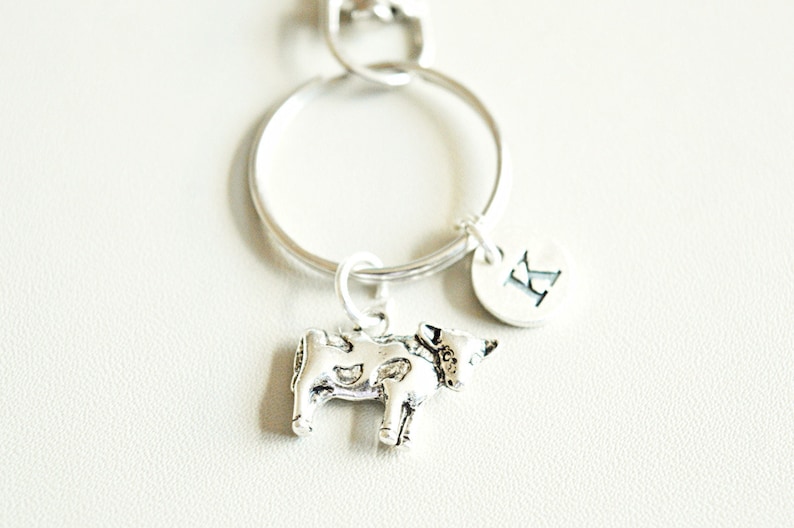 May include: Silver cow charm keychain with a silver initial charm with the letter K.