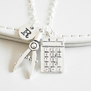 May include: Silver necklace with a calculator, compass, and initial charm. The initial charm is the letter "R".