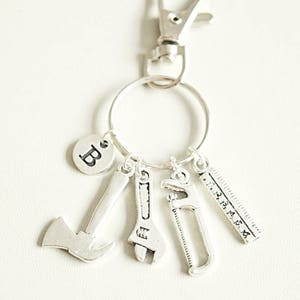 May include: Silver keychain with a letter B charm, a small axe, a wrench, a saw, and a ruler charm.