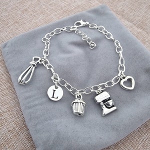 May include: Silver charm bracelet with a heart, a whisk, a cupcake, a mixer, and a letter L charm.