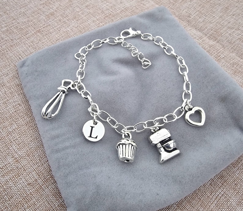 May include: Silver charm bracelet with a heart, a whisk, a cupcake, a mixer, and a letter L charm.