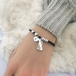 Puede incluir: Una pulsera el&aacute;stica negra con cuentas plateadas y un dije de un wicket de cricket y un disco plateado con la letra K.