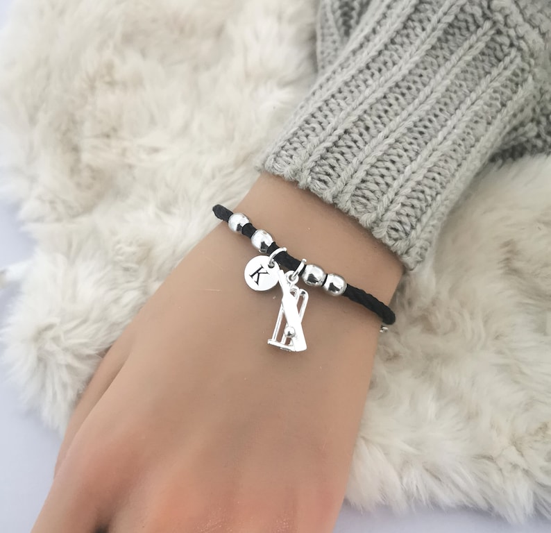 Puede incluir: Una pulsera el&aacute;stica negra con cuentas plateadas y un dije de un wicket de cricket y un disco plateado con la letra K.