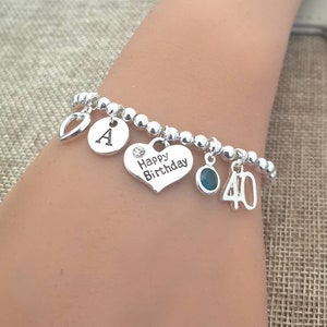 May include: Silver charm bracelet with a heart charm that says "Happy Birthday", a charm with the letter "A", a charm with a turquoise stone, and a charm with the number "40".