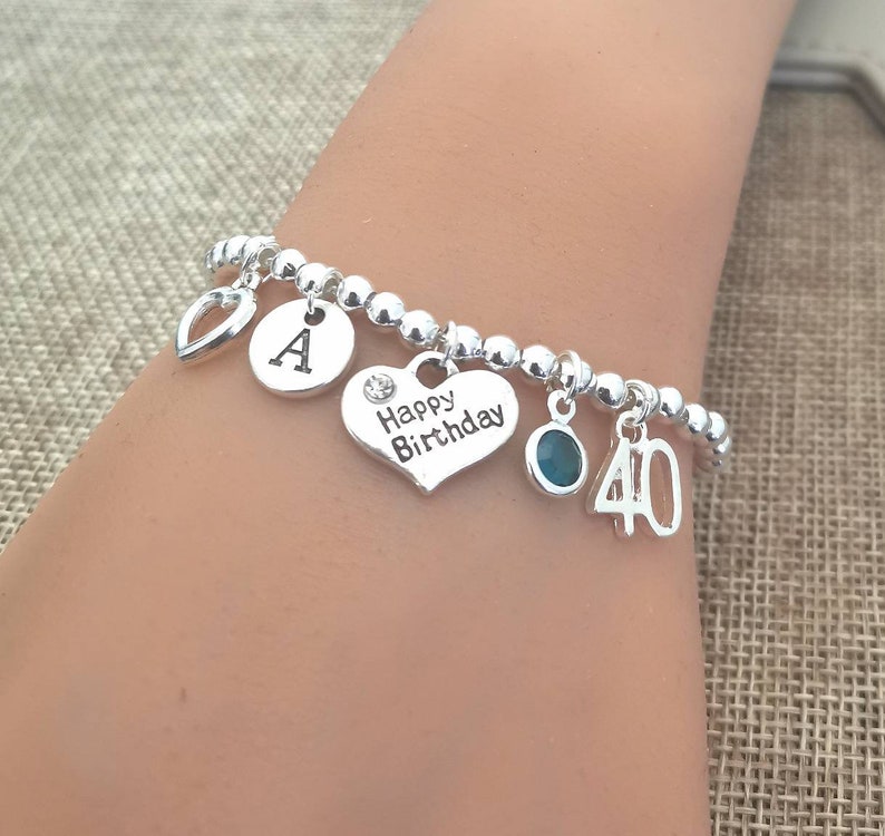 May include: Silver charm bracelet with a heart charm that says "Happy Birthday", a charm with the letter "A", a charm with a turquoise stone, and a charm with the number "40".