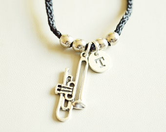 May include: A black braided cord necklace with silver beads and a silver trumpet charm. The charm has a small silver disc with the letter "T" engraved on it.