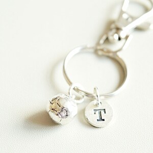 May include: Silver keychain with a small soccer ball charm and a letter 'T' charm.