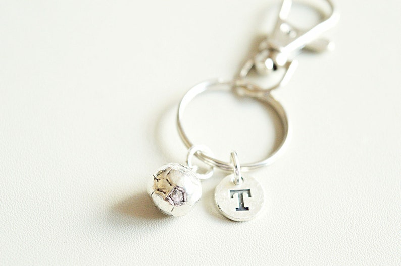 May include: Silver keychain with a small soccer ball charm and a letter 'T' charm.