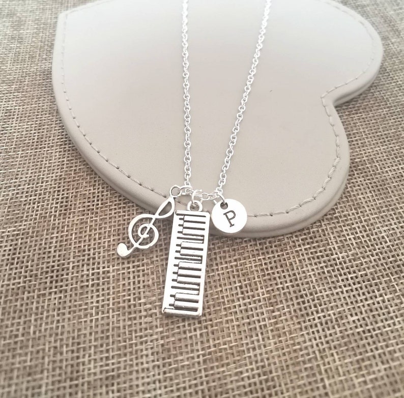 May include: Silver necklace with a piano keyboard charm, a treble clef charm, and a charm with the letter "P" hanging from it.