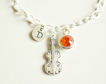 May include: A silver charm bracelet with a silver charm in the shape of a violin, a silver charm with the letter D, and a red crystal charm.