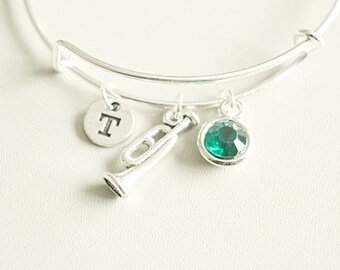 May include: Silver charm bracelet with a trumpet, a green gem, and a charm with the letter "T".