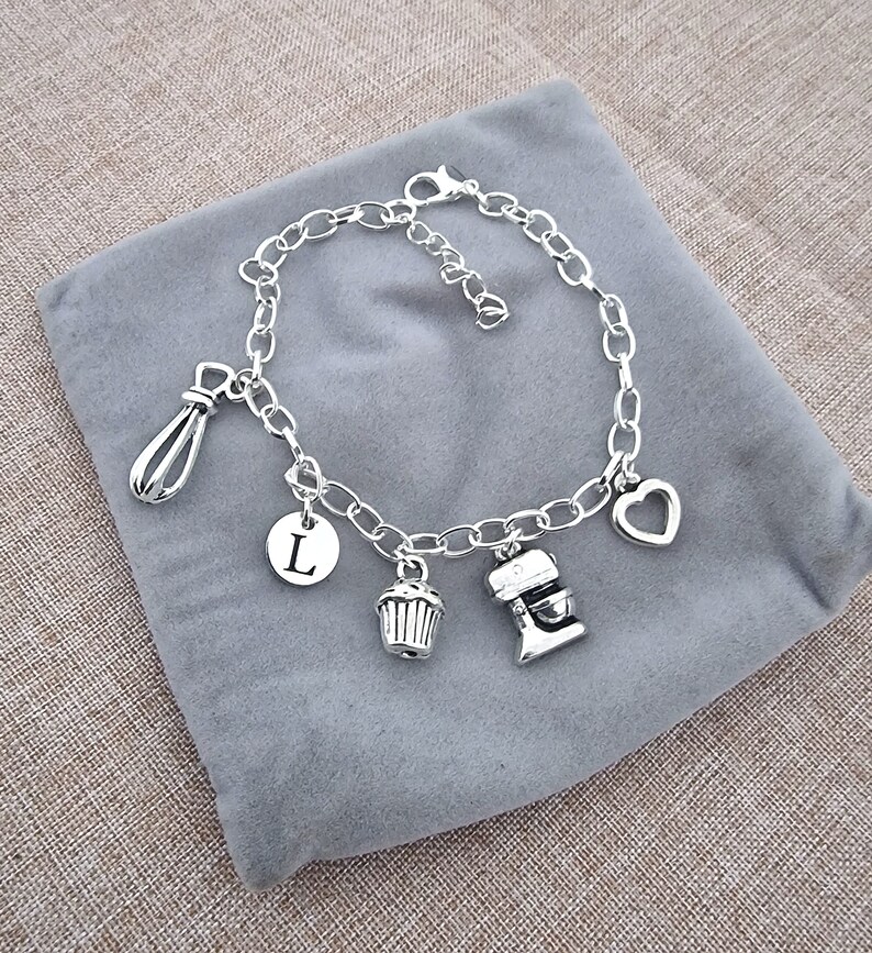 May include: Silver charm bracelet with a heart, cupcake, mixer, whisk, and initial L charm.