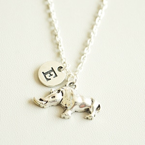 May include: A silver necklace with a small rhinoceros charm and a round charm with the letter 'E' on it.