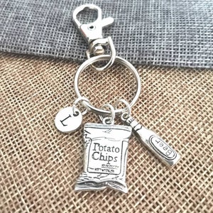 May include: Silver keyring with a charm of a bag of potato chips, a beer bottle charm, and a charm with the letter L.