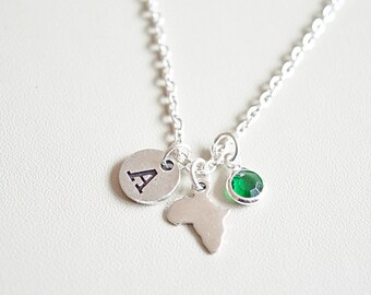 May include: Silver necklace with a charm of the continent of Africa, a green gemstone, and a silver charm with the letter A.