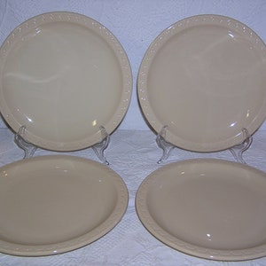 May include: Set of four cream-colored ceramic dinner plates with a raised rim and a decorative border.