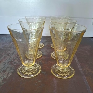 May include: Set of six vintage yellow glass sundae or dessert glasses. Each glass has a flared cone shape with a textured pattern and sits on a round, patterned base. The glasses are arranged on a dark surface.