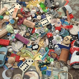 May include: A collection of various small objects, including dominoes, buttons, dice, a toy car, a cork with "WINERY" printed on it, and a miniature Pez dispenser. There is also a dollar bill and a watch.