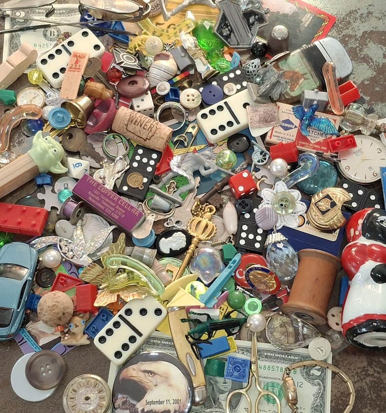 May include: A collection of various small objects, including dominoes, buttons, dice, a toy car, a cork with "WINERY" printed on it, and a miniature Pez dispenser. There is also a dollar bill and a watch.