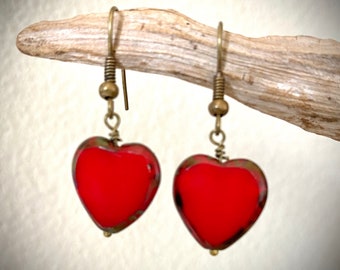 May include: A pair of red heart-shaped dangle earrings with gold-toned metal hooks.