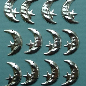 May include: Twelve silver crescent moon ornaments with a star and a face on each. The ornaments are all the same size and shape.