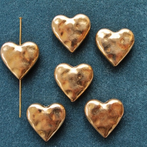 May include: Six gold heart-shaped charms with a textured surface. The charms are arranged in a semi-circle on a blue background.