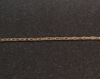 May include: A gold chain with a box link pattern. The chain is on a black background.